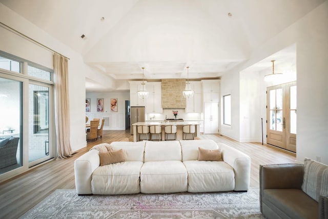 living room with an inviting chandelier, light hardwood / wood-style flooring, and high vaulted ceiling