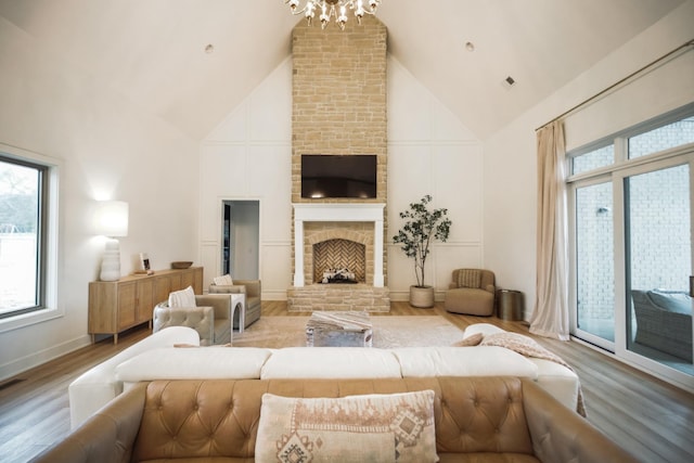 living room featuring an inviting chandelier, a fireplace, high vaulted ceiling, and light wood-type flooring