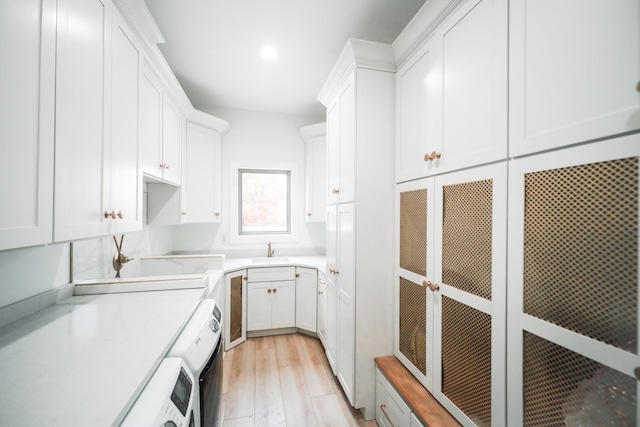 laundry area with sink, washer and clothes dryer, cabinets, beverage cooler, and light wood-type flooring