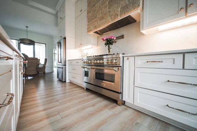 kitchen featuring high quality appliances, light hardwood / wood-style floors, white cabinets, decorative light fixtures, and wall chimney exhaust hood