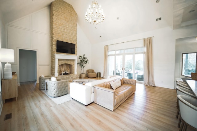 living room with high vaulted ceiling, an inviting chandelier, a fireplace, and light hardwood / wood-style floors