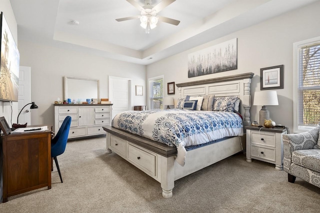 bedroom featuring light colored carpet, a raised ceiling, and ceiling fan