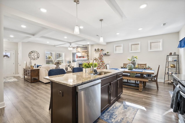 kitchen with sink, hanging light fixtures, a center island with sink, stainless steel dishwasher, and a fireplace