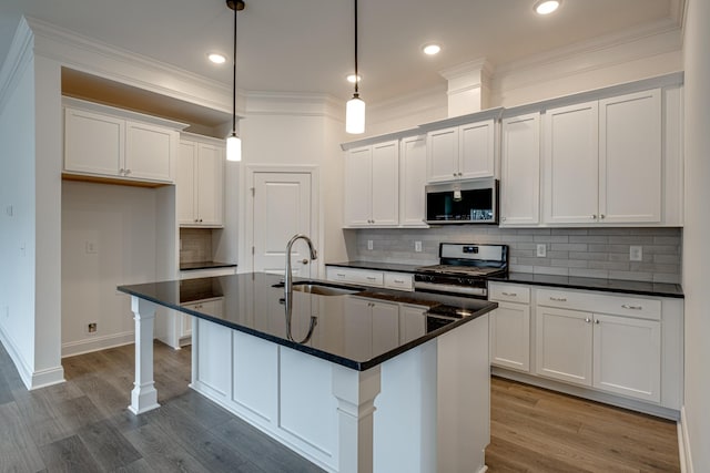 kitchen featuring sink, appliances with stainless steel finishes, white cabinetry, a center island with sink, and decorative light fixtures