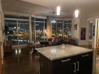 kitchen with light stone counters, decorative light fixtures, dark wood-type flooring, and a center island