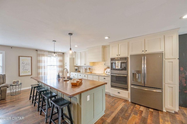 kitchen featuring appliances with stainless steel finishes, decorative light fixtures, white cabinets, dark hardwood / wood-style flooring, and a kitchen island with sink