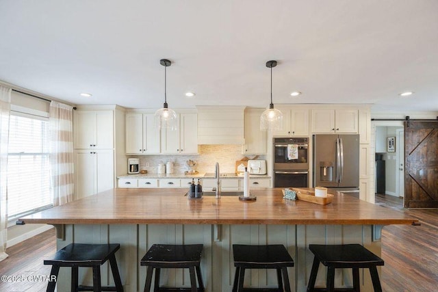 kitchen with tasteful backsplash, a center island with sink, appliances with stainless steel finishes, pendant lighting, and a barn door