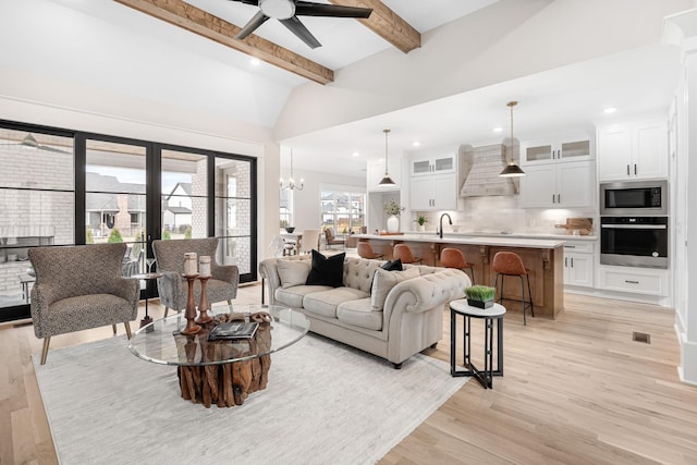 living room with lofted ceiling with beams, ceiling fan with notable chandelier, light hardwood / wood-style floors, and sink