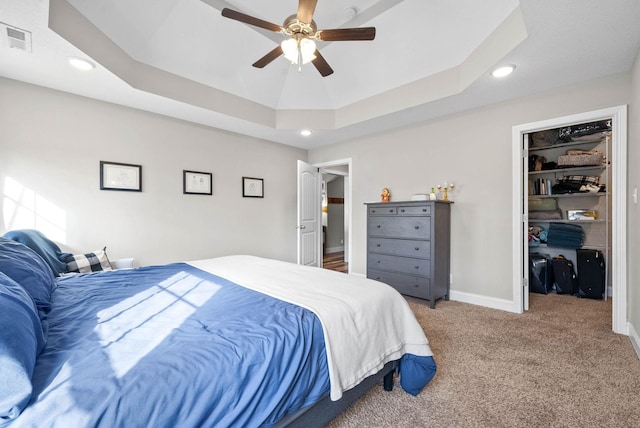 carpeted bedroom with a tray ceiling, ceiling fan, a walk in closet, and a closet