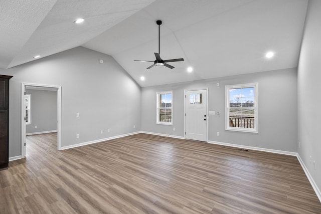 unfurnished living room with vaulted ceiling, a healthy amount of sunlight, ceiling fan, and light wood-type flooring