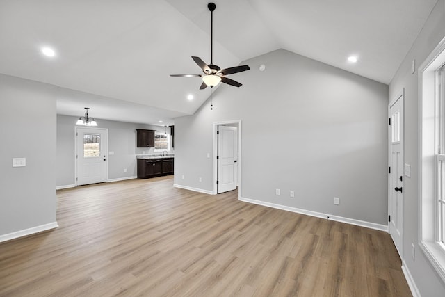 unfurnished living room featuring ceiling fan with notable chandelier, high vaulted ceiling, and light wood-type flooring