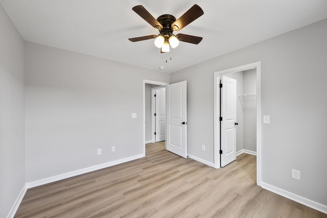 unfurnished bedroom featuring ceiling fan, a spacious closet, a closet, and light hardwood / wood-style flooring