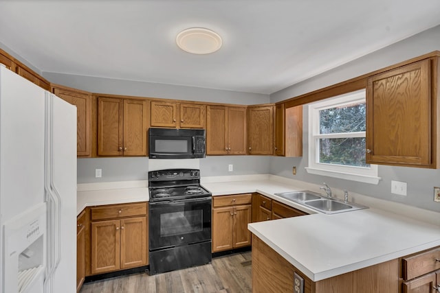 kitchen with sink, black appliances, light hardwood / wood-style floors, and kitchen peninsula