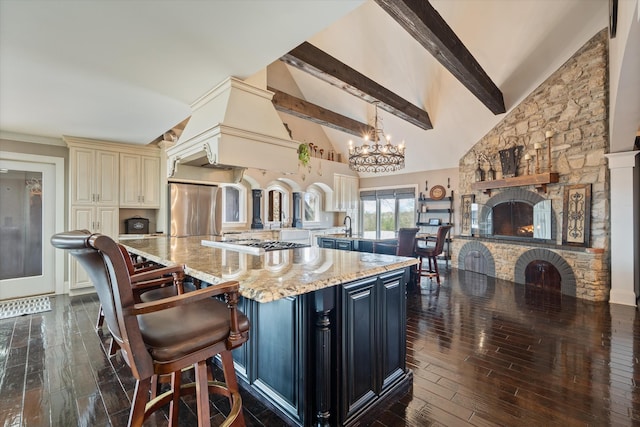 kitchen featuring a kitchen island, appliances with stainless steel finishes, hanging light fixtures, a stone fireplace, and a kitchen bar