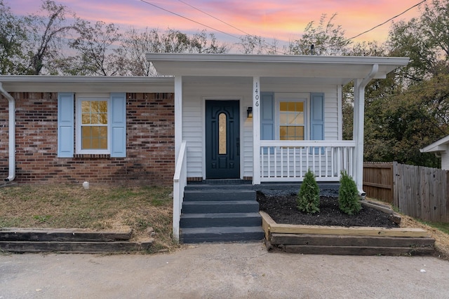 view of front of home featuring covered porch, brick siding, and fence