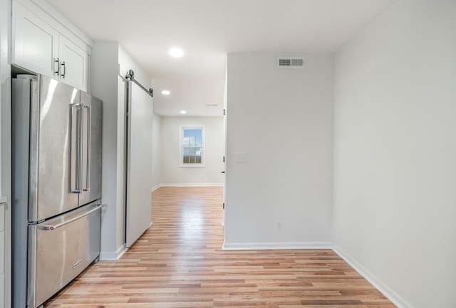 kitchen with a barn door, visible vents, white cabinets, light wood-style flooring, and high end fridge