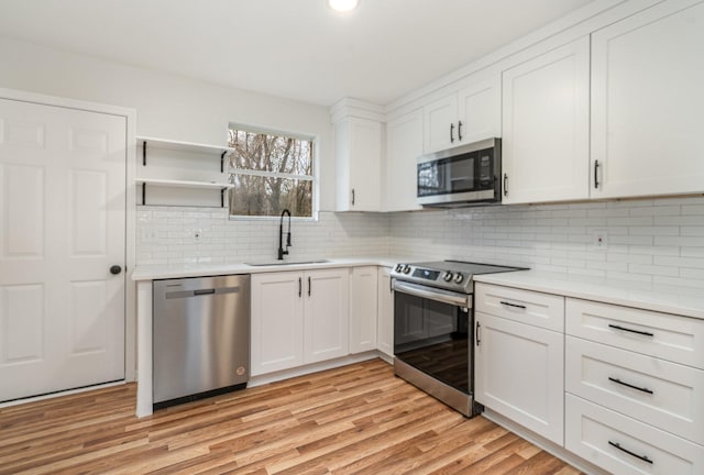 kitchen with light wood finished floors, appliances with stainless steel finishes, light countertops, and a sink