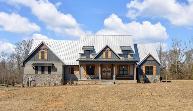 modern farmhouse featuring stone siding, a standing seam roof, covered porch, board and batten siding, and a front yard