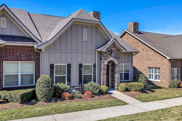 view of front of home with a shingled roof, a front yard, stone siding, board and batten siding, and a chimney