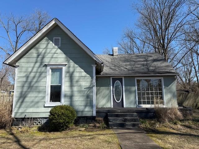 view of front of property with a shingled roof, a chimney, and fence