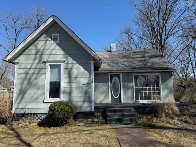 view of front of property with a chimney, fence, and roof with shingles