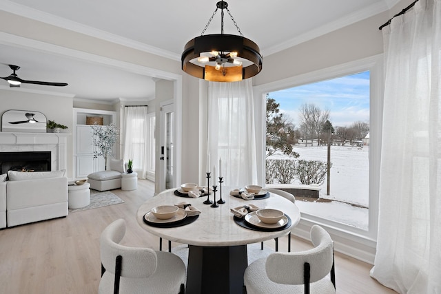 dining space with ceiling fan with notable chandelier, light wood-style floors, a fireplace, and crown molding