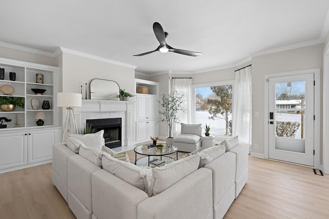 living area featuring a tiled fireplace, ceiling fan, light wood-type flooring, and crown molding