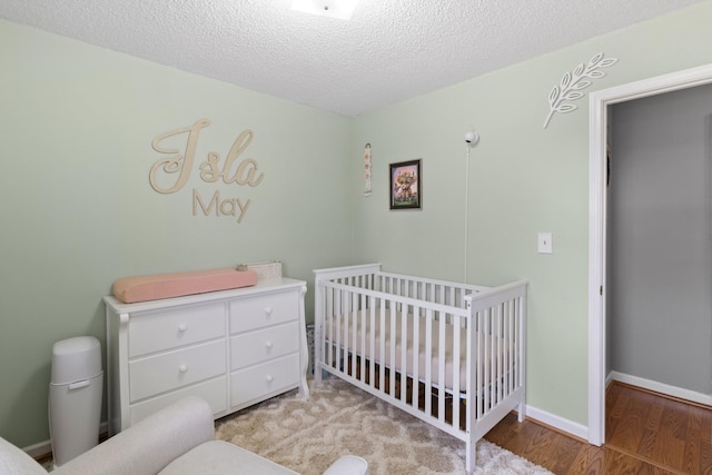 bedroom with a nursery area, light wood-type flooring, and a textured ceiling