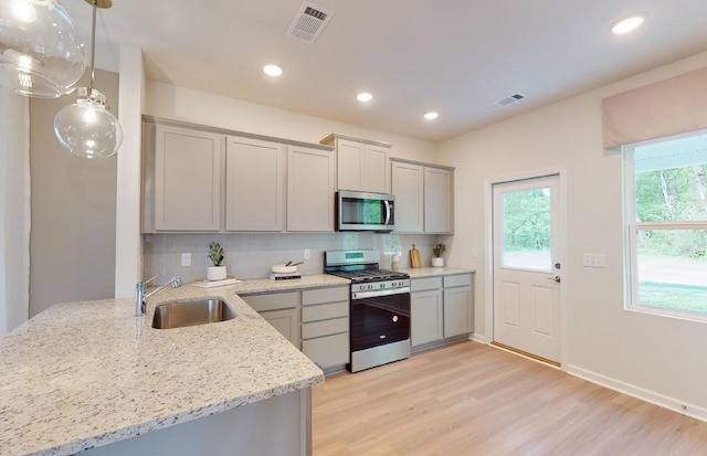 kitchen with appliances with stainless steel finishes, pendant lighting, sink, gray cabinetry, and light stone counters