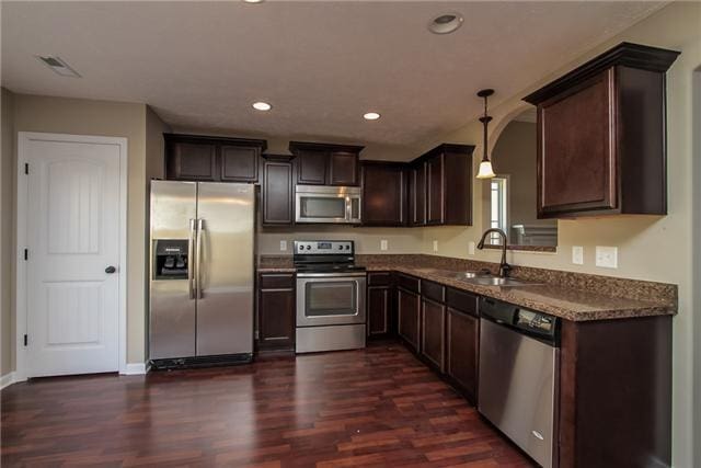 kitchen featuring sink, hanging light fixtures, appliances with stainless steel finishes, dark hardwood / wood-style flooring, and dark stone counters