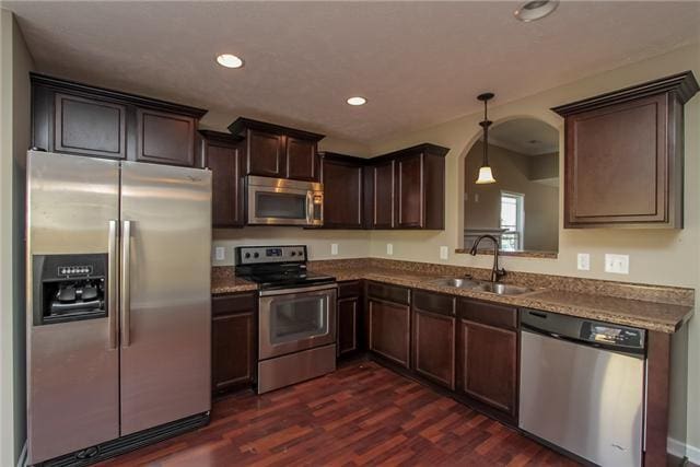 kitchen featuring pendant lighting, sink, stone counters, stainless steel appliances, and dark hardwood / wood-style flooring