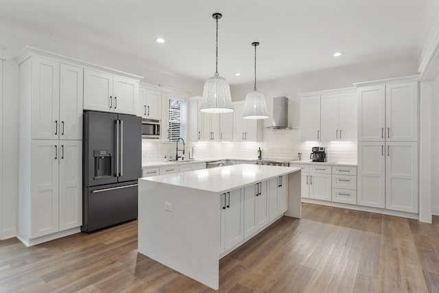 kitchen with wall chimney range hood, a kitchen island, white cabinets, and appliances with stainless steel finishes