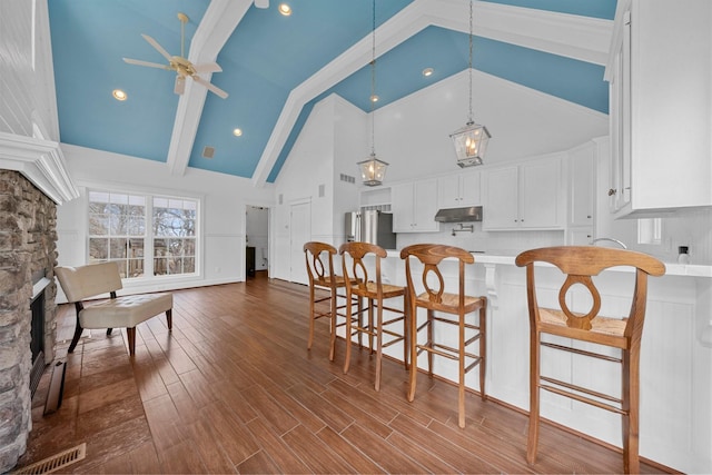 kitchen with stainless steel fridge, hardwood / wood-style floors, white cabinets, and decorative light fixtures