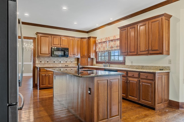 kitchen featuring stainless steel refrigerator, dark hardwood / wood-style floors, light stone counters, and a center island with sink