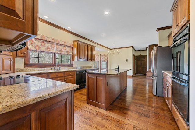 kitchen featuring light stone counters, hanging light fixtures, an island with sink, hardwood / wood-style flooring, and black appliances