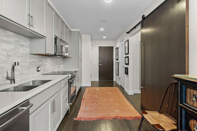 kitchen with sink, dark wood-type flooring, appliances with stainless steel finishes, tasteful backsplash, and a barn door