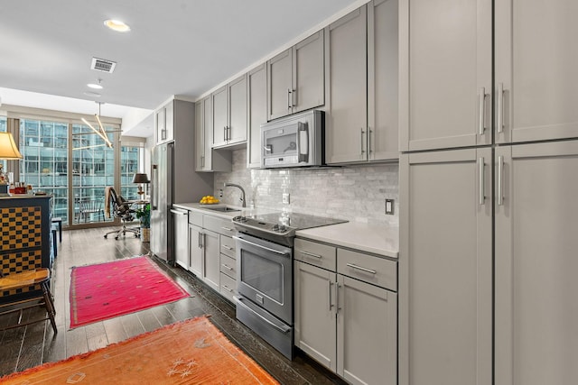 kitchen with sink, gray cabinets, appliances with stainless steel finishes, dark hardwood / wood-style floors, and tasteful backsplash