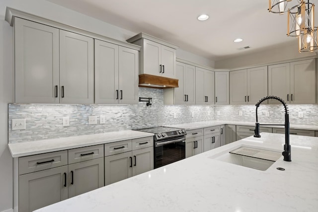 kitchen featuring stainless steel electric range, a sink, decorative light fixtures, and light stone countertops