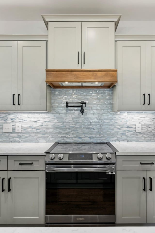 kitchen featuring light stone counters, gray cabinetry, electric stove, decorative backsplash, and custom range hood