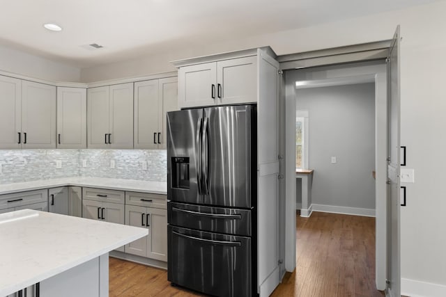 kitchen featuring decorative backsplash, light wood-style floors, light stone countertops, stainless steel fridge, and baseboards