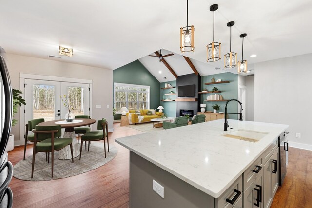 kitchen featuring a ceiling fan, a glass covered fireplace, vaulted ceiling, a sink, and wood finished floors