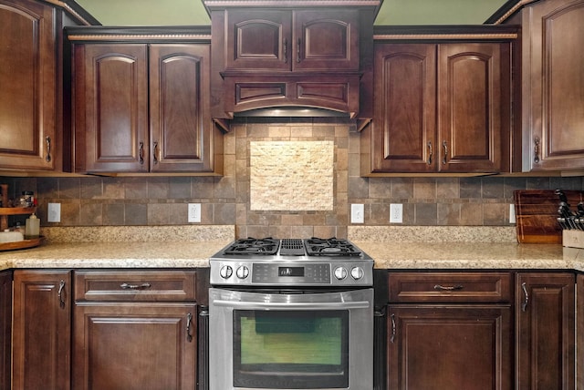 kitchen with light stone counters, decorative backsplash, stainless steel gas range, and dark brown cabinets