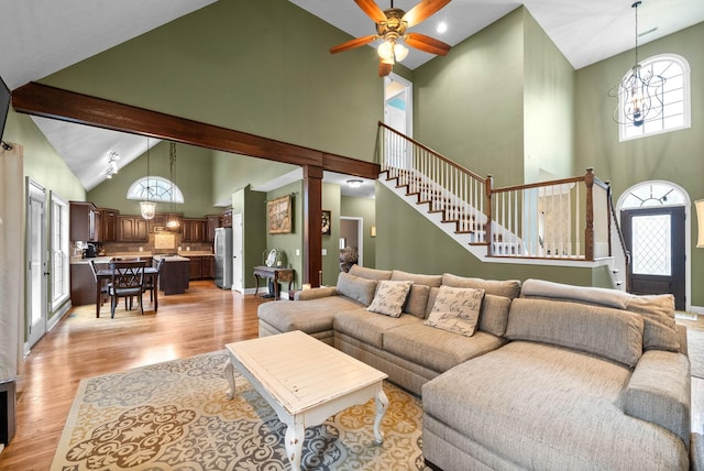 living room featuring ceiling fan with notable chandelier, beam ceiling, high vaulted ceiling, and light wood-type flooring