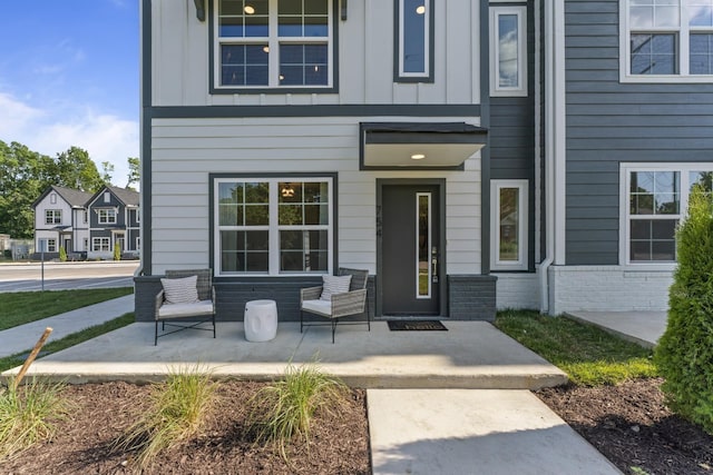 doorway to property featuring board and batten siding, covered porch, and brick siding