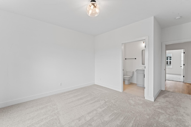 unfurnished bedroom featuring ensuite bath, baseboards, and light colored carpet