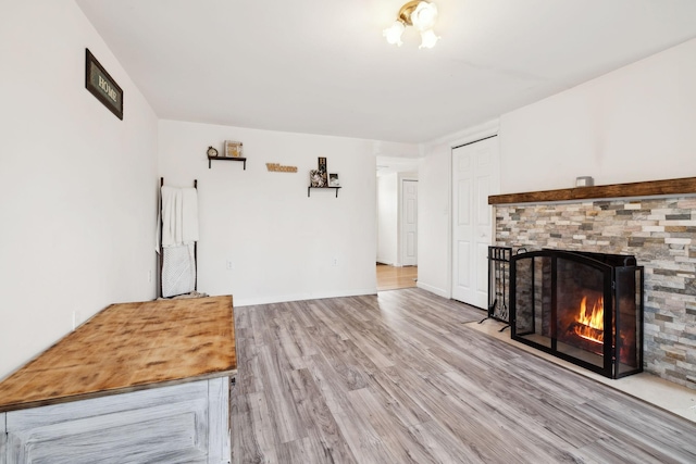 unfurnished living room with a warm lit fireplace, baseboards, and wood finished floors