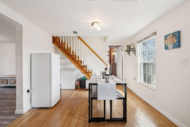 dining room featuring light wood-type flooring, visible vents, baseboards, and stairs