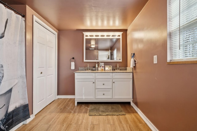 full bathroom featuring double vanity, baseboards, a sink, and wood finished floors