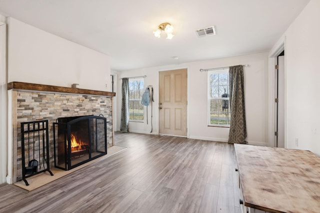 unfurnished living room featuring baseboards, a lit fireplace, visible vents, and wood finished floors