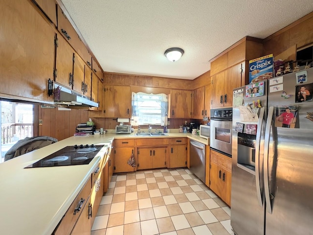 kitchen with stainless steel appliances, wood walls, a textured ceiling, and sink